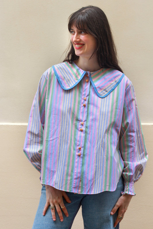 Woman wearing a pastel striped blouse with a blue collar against a beige background